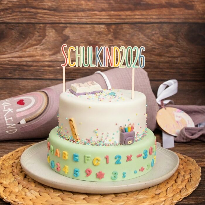 Festlich gedeckte Kaffeetafel zur Einschulung 2026 mit einer Torte, die durch einen farbig bedruckten Holz-Cake Topper Schulkind der Marke 'von Mia' verziert ist.