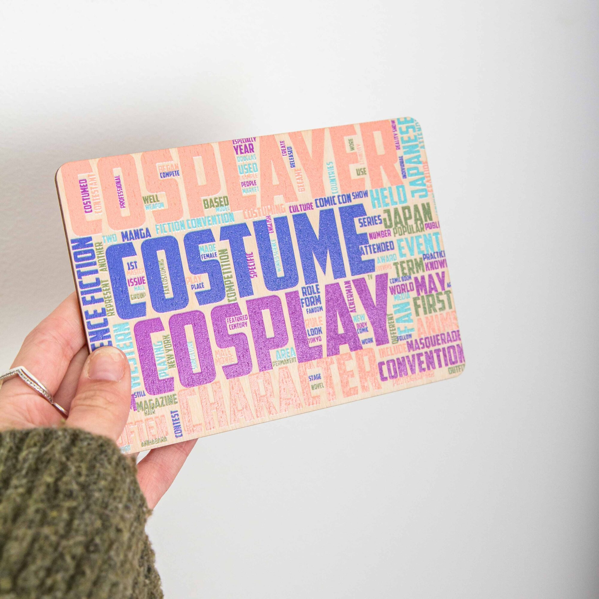 Postkarte Cosplay / Holzpostkarte Bücherliebhaber / Bookstagram / Postkarten mit Botschaft 2 Eine rechteckige Holzpostkarte im Querformat. Im Zentrum stechen vier Begriffe in sehr großen, strukturierten Großbuchstaben hervor: „COSPLAYER“ in Lachsrosa ganz oben, „COSTUME“ in Dunkelblau darunter, gefolgt von „COSPLAY“ in Lila und „CHARACTER“ in hellem Orange am unteren Rand. Die Zwischenräume und Ränder sind dicht mit kleineren, zugehörigen englischen Begriffen wie „Manga“, „Anime“, „Convention“, „Japan“ und „Science Fiction“ in verschiedenen Farben und Ausrichtungen gefüllt.