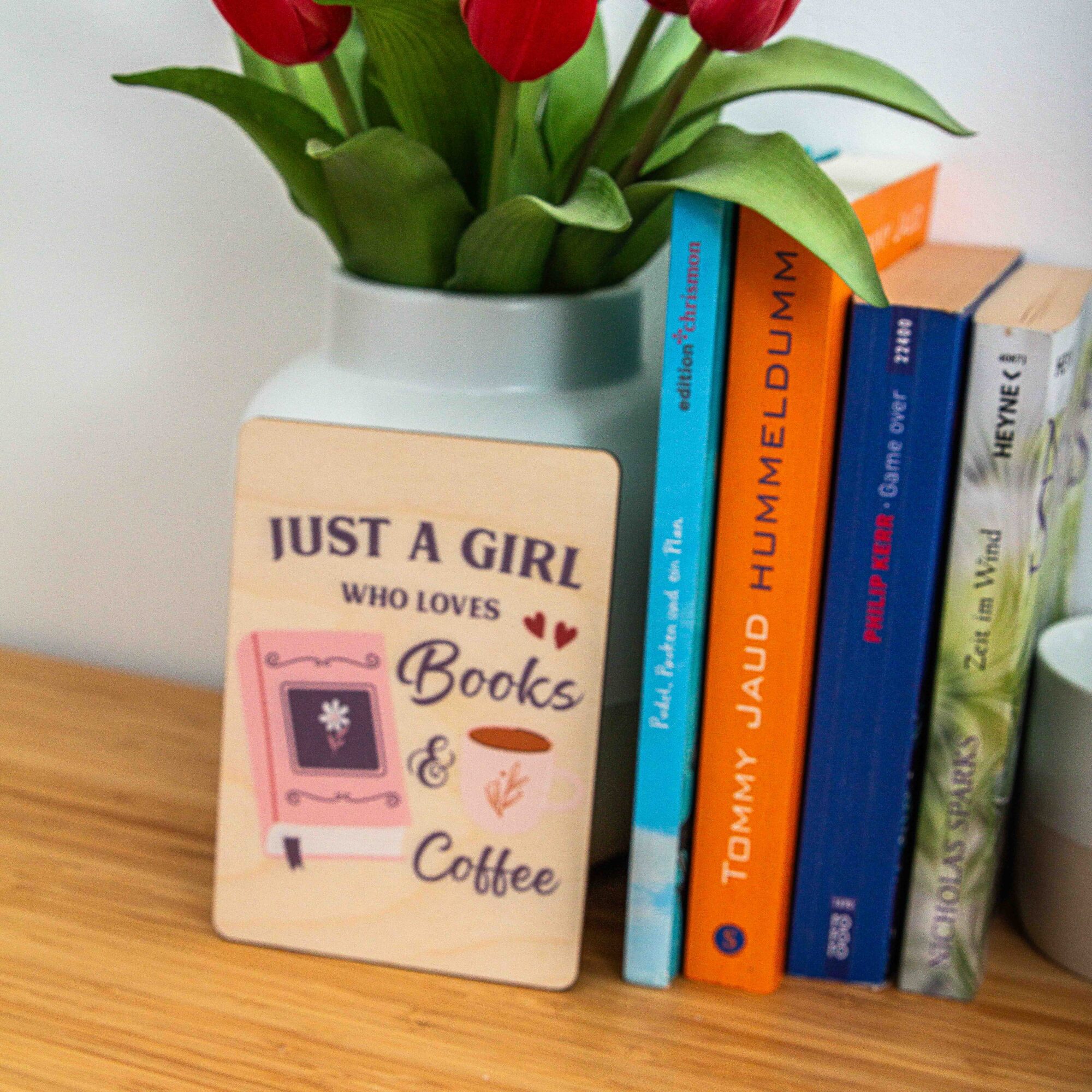 Postkarte Just a girl who loves books and coffee / Holzpostkarte Bücherliebhaber / Bookstagram / Postkarten mit Botschaft 4 Eine rechteckige Holzpostkarte liegt flach auf einer hellbraunen Holzoberfläche mit deutlicher Maserung. Auf der Karte ist ein lila und rosa Grafikdesign mit dem englischen Spruch „JUST A GIRL WHO LOVES Books & Coffee“ aufgedruckt. Links neben dem Text „Books“ ist ein geschlossenes, rosa Buch mit einer kleinen Blume auf dem Cover und einem lila Lesebändchen abgebildet. Rechts neben dem Wort „Coffee“ ist eine weiße Kaffeetasse mit einer kleinen Pflanzen-Illustration zu sehen.