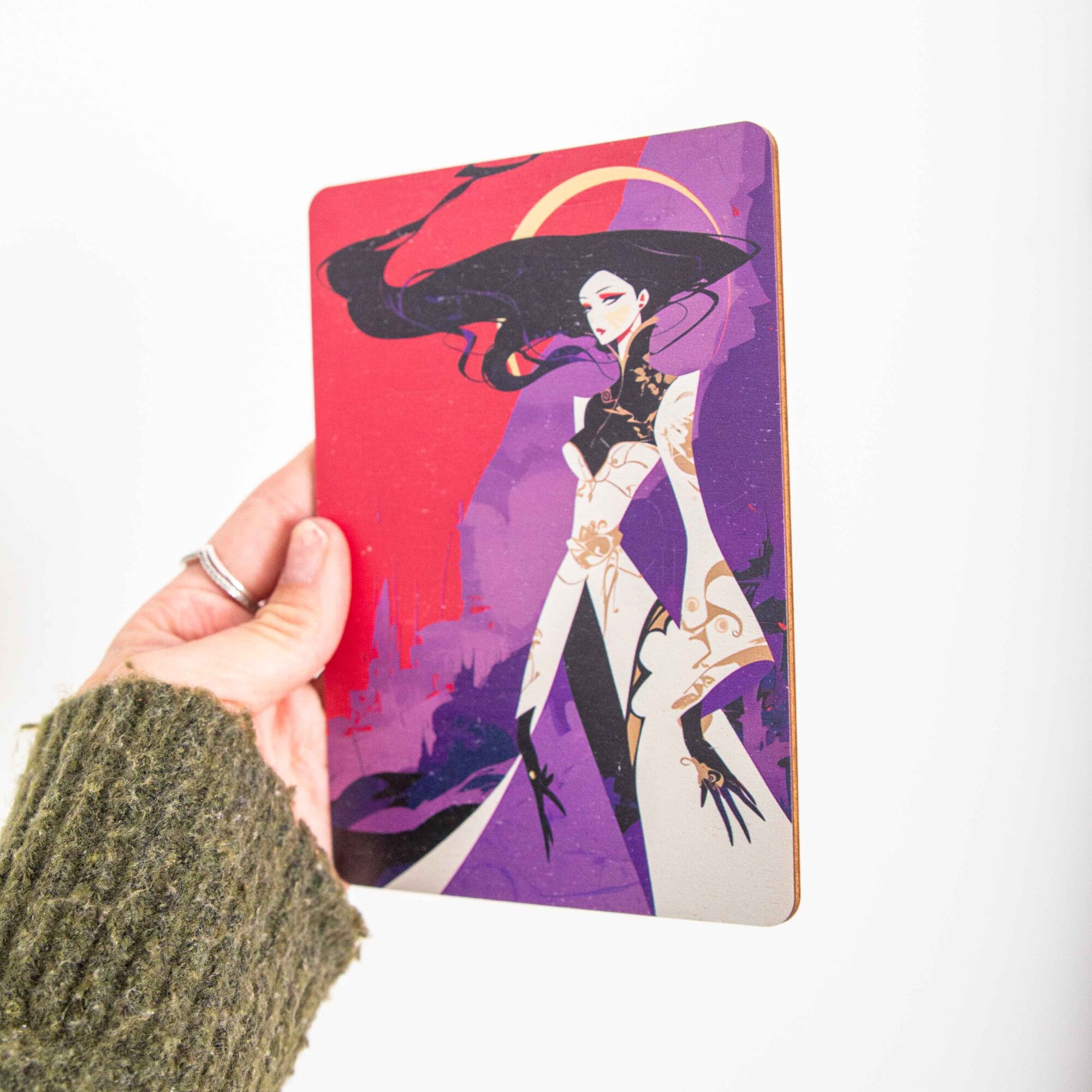 Postkarte Anime / Holzpostkarte Bücherliebhaber / Bookstagram / Postkarten mit Botschaft 2 Eine rechteckige Holzpostkarte im Hochformat liegt flach auf einer hellbraunen Holzoberfläche. Die Karte zeigt eine vollflächige, dramatische Fantasy-Illustration im modernen, kantigen Graphic-Novel-Stil. Im Zentrum steht eine elegante weibliche Figur mit extrem langem, fließendem schwarzen Haar und auffälligem roten Make-up. Sie trägt ein stilisiertes weißes Gewand mit goldenen Ornamenten und weiten Ärmeln, kombiniert mit schwarzen Elementen und langen, spitzen Fingern.