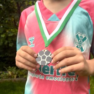 Mitarbeitergeschenke 38 Ein Kind im Fußballtrikot hält stolz eine handgemachte, runde Holzmedaille aus Birkenholz in den Händen.